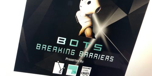 A photograph of a monitor showing the Bots Breaking Barriers poster